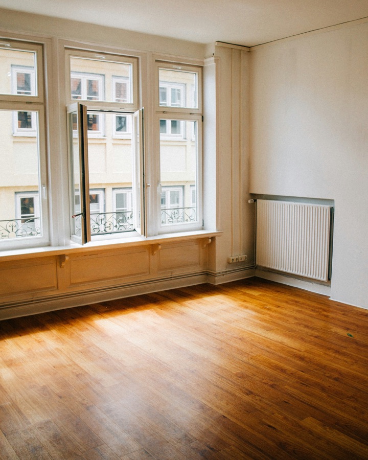 Empty apartment room with bare wooden floor and radiator before furnishing
