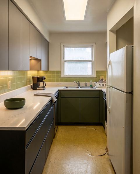 The same galley kitchen redesigned in modern style with handleless charcoal base cabinets, warm grey upper doors, an olive sink cabinet, a white quartz countertop and warm under-cabinet lighting
