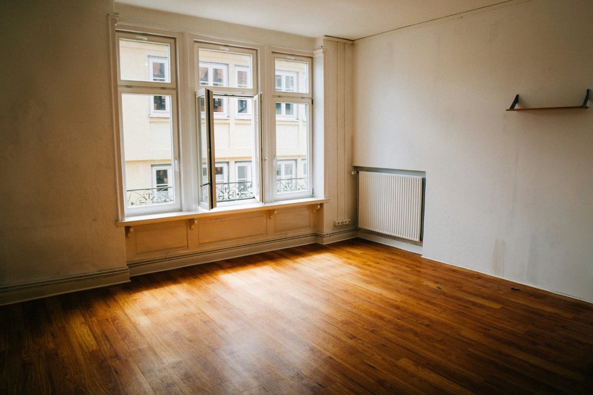 Une pièce vide avec de hautes fenêtres, un radiateur et un parquet